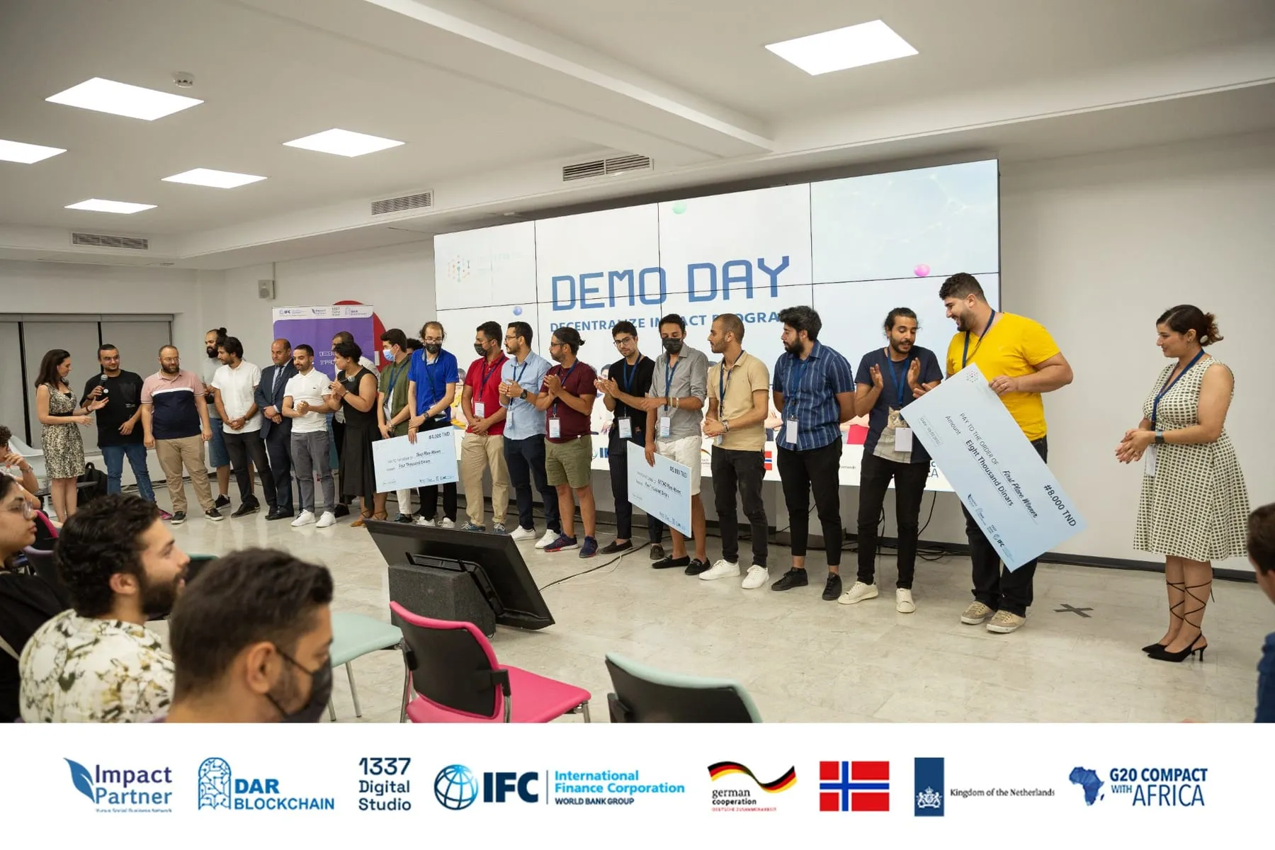 Decentralize Impact demo day winners on stage holding their award cheques