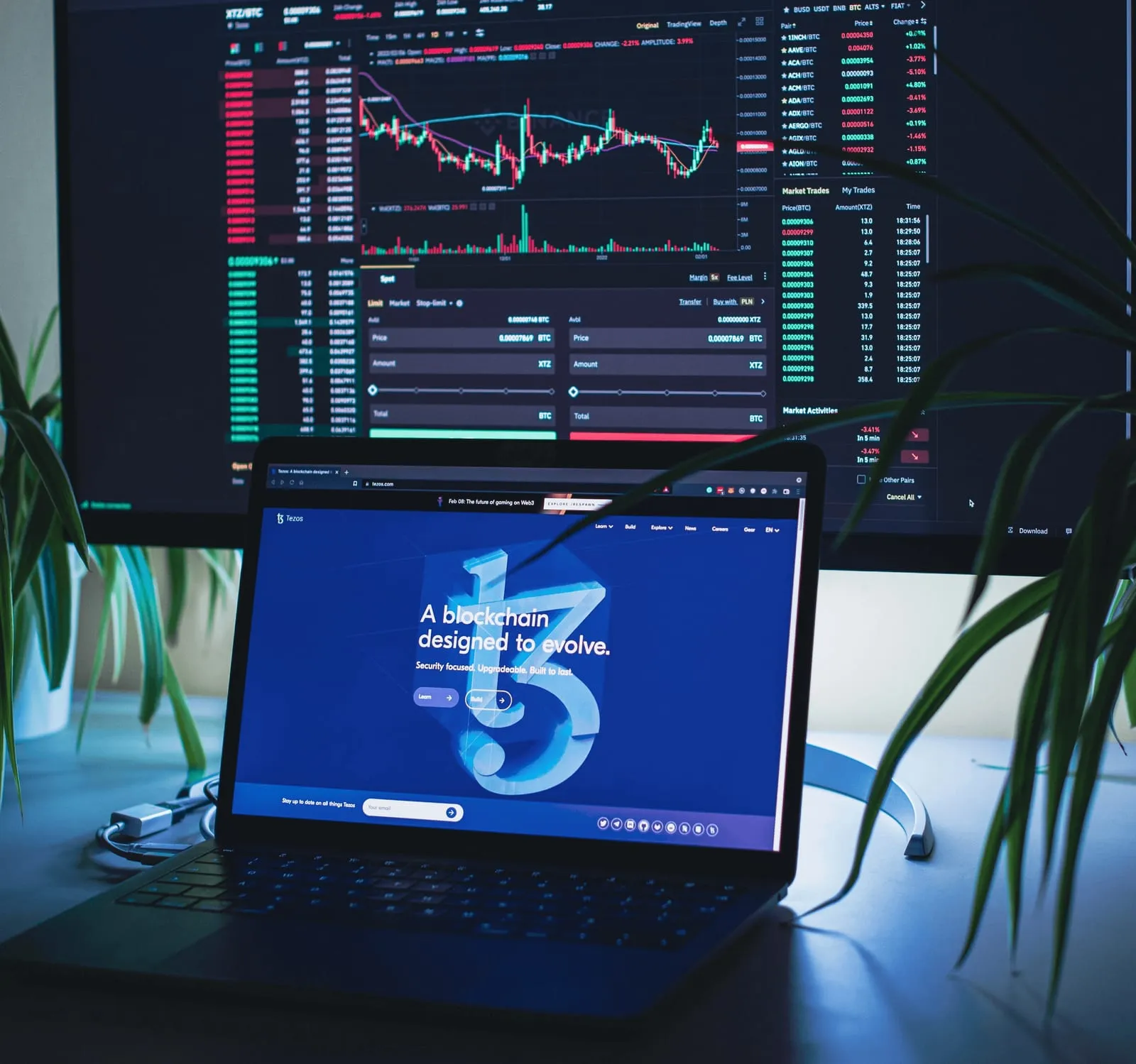Trading dashboards on a monitor and a laptop showing a blockchain landing page
